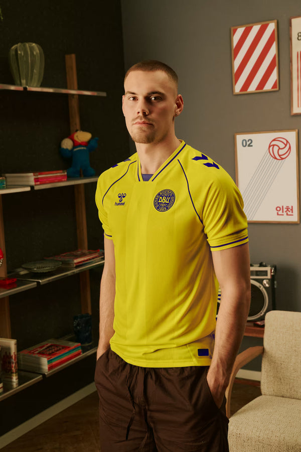 Man wearing a bright yellow DUB jersey in a room with shelves and decor.